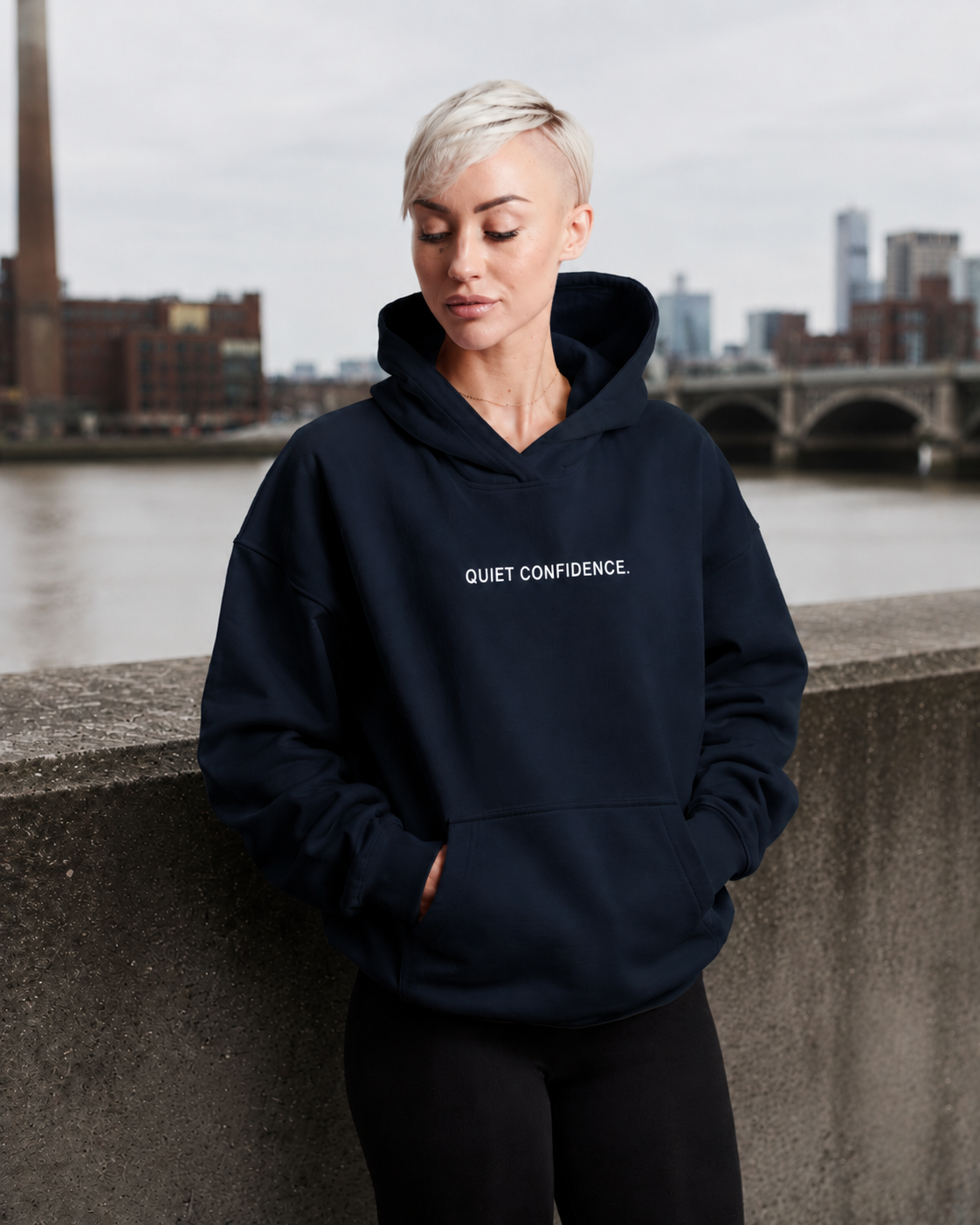 French navy oversized Quiet Confidence hoodie on female model in London riverside streetwear scene.