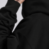 Close-up detail shot of a heavyweight black hoodie showing premium shoulder seam construction, ribbed cuff texture, and soft brushed fabric finish. Minimal studio lighting highlights the quality stitching, dense material, and oversized streetwear craftsmanship.