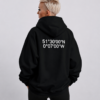 Oversized black hoodie with white London coordinates back print, shown in a relaxed waist-up pose. Model turned slightly away from camera to highlight the oversized drape, dropped shoulders, and heavyweight silhouette against a clean neutral studio background.