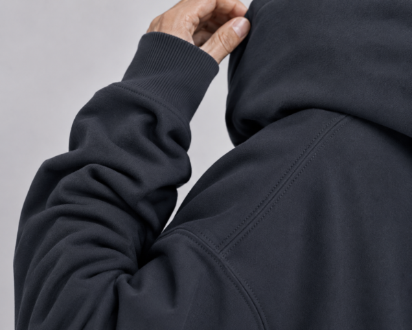 kk-hoodie-london-india- ink-grey-fabric Detailed fabric close-up of India ink grey oversized hoodie showing heavyweight organic cotton texture, shoulder seam detail, ribbed cuff, and premium construction