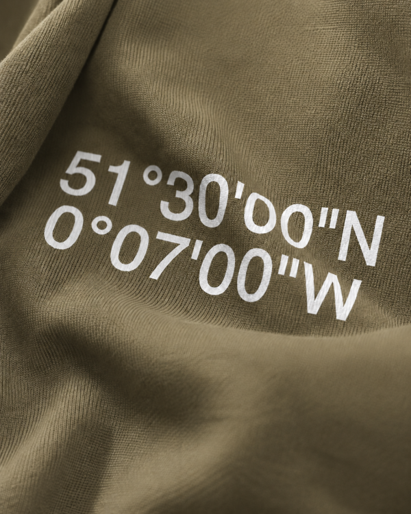 kk-hoodie-london-khaki-close-design Close-up of Khaki oversized hoodie with London coordinates back print in white typography. Heavyweight cotton fabric texture and premium print detail shown in soft editorial lighting.