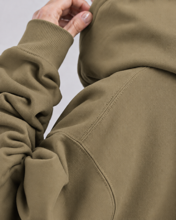 kk-hoodie-london-khaki-close-fabric Detailed fabric close-up of Khaki oversized streetwear hoodie showing heavyweight cotton texture, shoulder seam construction, ribbed cuff, and premium minimal finish.