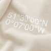Close-up of Natural Raw oversized hoodie with London coordinates back print in minimalist typography. Premium heavyweight cotton texture and detailed print finish shown in editorial lighting.