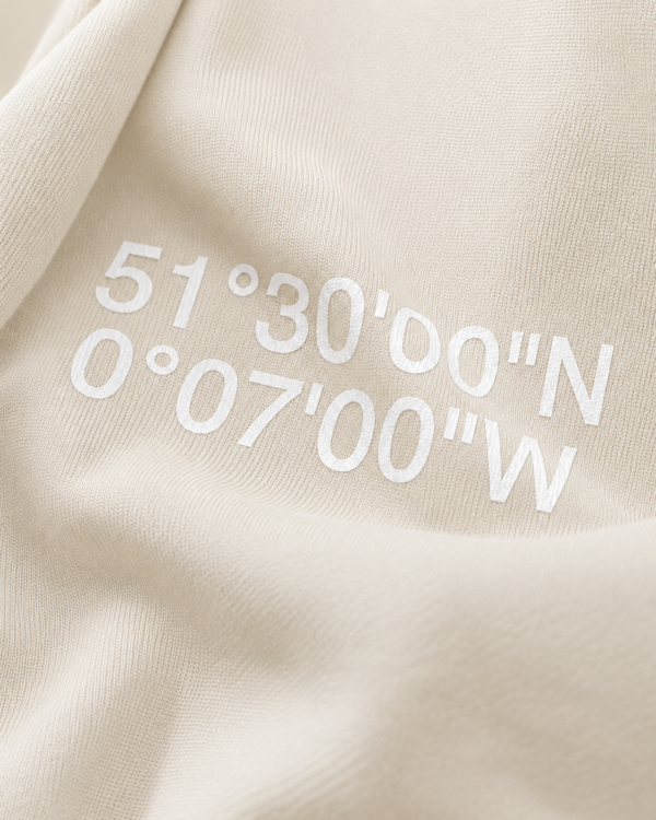 Close-up of Natural Raw oversized hoodie with London coordinates back print in minimalist typography. Premium heavyweight cotton texture and detailed print finish shown in editorial lighting.