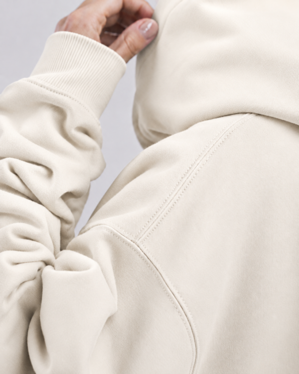 Detailed fabric close-up of Natural Raw oversized hoodie showing heavyweight organic cotton texture, shoulder seam detail, ribbed cuff, and premium construction