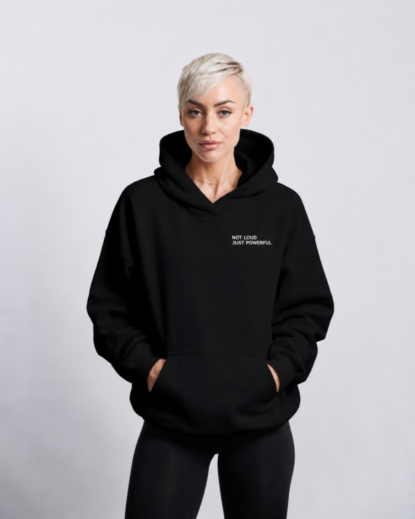 kk-hoodie-not-loud-just-powerful-front-logo-black Front view of oversized black minimalist hoodie with subtle white “NOT LOUD JUST POWERFUL” chest logo, heavyweight premium fabric, kangaroo pocket, and relaxed modern streetwear fit against a neutral studio background.