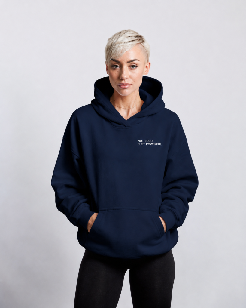 Front view of oversized French navy minimalist hoodie with small white “NOT LOUD JUST POWERFUL” chest logo, premium heavyweight fabric, kangaroo pocket, and relaxed oversized silhouette in a modern studio setting.