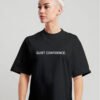 kk-tee-Quiet-Confidence-black-g-kk Woman wearing black oversized Quiet Confidence T-Shirt by Kat Krush against a light grey background