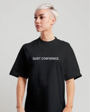 Woman wearing black oversized Quiet Confidence T-Shirt by Kat Krush against a light grey background