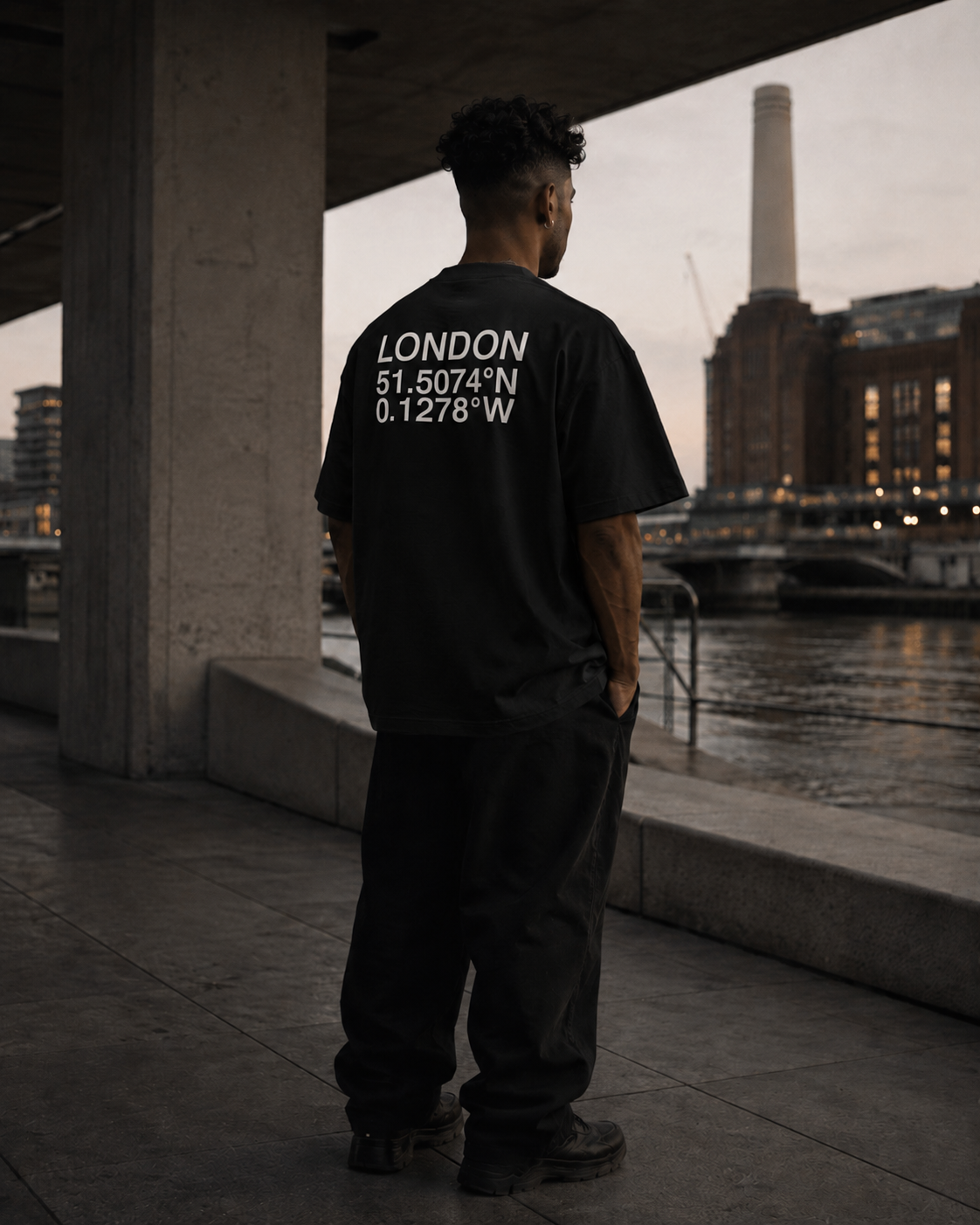 Black oversized London Coordinates t-shirt photographed within a modern concrete architectural setting overlooking the Thames in London.