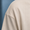 kk-tee-minimal-noise-max-impact-closeup-fabric-natural-raw Close-up of the shoulder, sleeve and ribbed collar of a natural raw oversized T-shirt, highlighting the smooth heavyweight cotton fabric, clean stitching and relaxed dropped-shoulder construction.