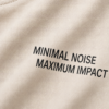 kk-tee-minimal-noise-max-impact-front-print-natural-raw Detailed close-up of the chest area of a natural raw oversized T-shirt featuring the minimalist slogan “MINIMAL NOISE MAXIMUM IMPACT” printed in black. The image showcases fabric texture, print quality and premium construction.