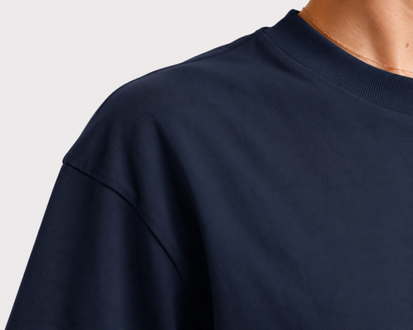 Close-up of the shoulder and neckline of a French navy oversized t-shirt showing heavyweight cotton texture, dropped shoulder construction, and premium ribbed collar detail.