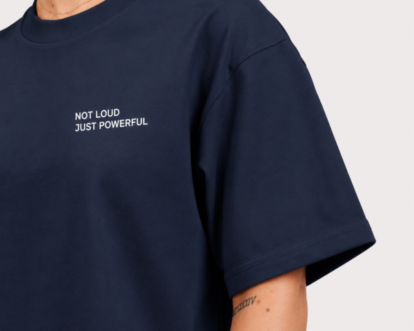 Detailed close-up of oversized French navy t-shirt featuring minimalist “NOT LOUD JUST POWERFUL” chest print, smooth heavyweight fabric texture, and wide sleeve construction.