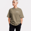 Oversized khaki Kat Krush t-shirt featuring minimalist “NOT LOUD JUST POWERFUL” chest print, styled in a relaxed studio fashion pose with soft neutral streetwear tones.