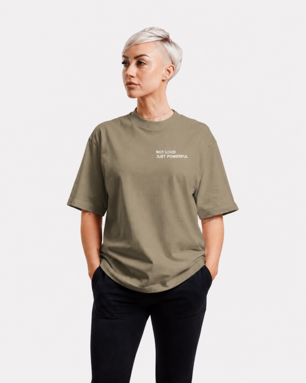 Oversized khaki Kat Krush t-shirt featuring minimalist “NOT LOUD JUST POWERFUL” chest print, styled in a relaxed studio fashion pose with soft neutral streetwear tones.
