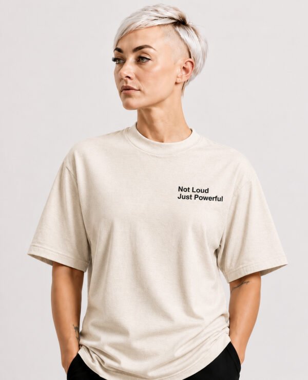 Close-up portrait of a model wearing a natural raw oversized Kat Krush T-shirt featuring the “Not Loud Just Powerful” chest print, highlighting the relaxed fit and premium fabric texture.