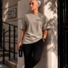 Model wearing a stone oversized Kat Krush T-shirt with “Not Loud Just Powerful” chest print, leaning against a London townhouse exterior in a quiet urban setting.