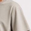 Close-up of the shoulder, sleeve and fabric texture of a stone Kat Krush oversized T-shirt, highlighting the heavyweight material, stitching and garment construction.