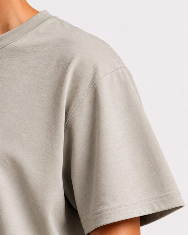 Close-up of the shoulder, sleeve and fabric texture of a stone Kat Krush oversized T-shirt, highlighting the heavyweight material, stitching and garment construction.
