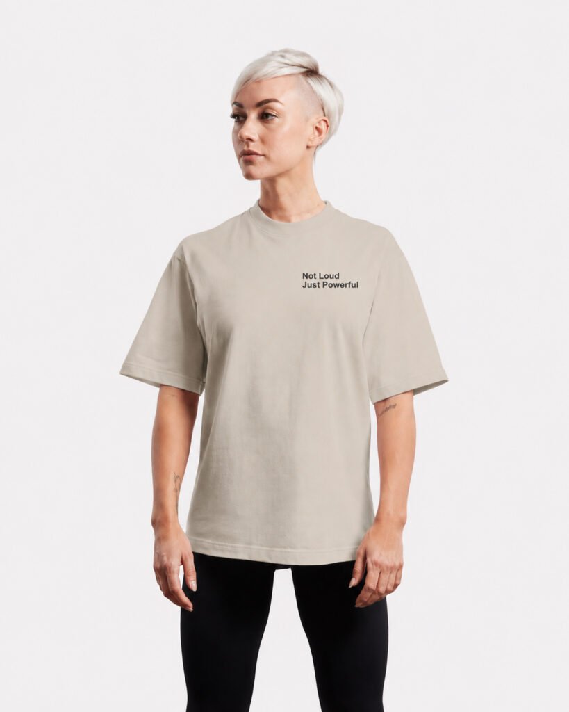 Front-facing studio image of a stone oversized Kat Krush T-shirt featuring a minimalist “Not Loud Just Powerful” chest print and relaxed oversized silhouette.