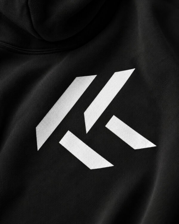Close-up studio portrait of a black Kat Krush oversized hoodie featuring the white KK chest logo, premium heavyweight fabric, and clean minimalist aesthetic.
