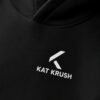 Close-up of black Kat Krush oversized hoodie showing white chest logo print and heavyweight cotton fabric texture. Premium minimal streetwear detail.