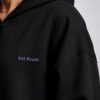Detailed close-up of lilac Kat Krush chest logo on black oversized hoodie. Premium heavyweight cotton fabric with clean minimal branding and dropped shoulder construction.