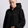 Black oversized Kat Krush hoodie with subtle lilac chest logo. Relaxed heavyweight fit with kangaroo pocket and contemporary minimal streetwear silhouette.