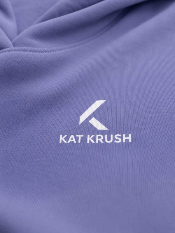 Close-up of the white Kat Krush chest logo printed on violet hoodie fabric