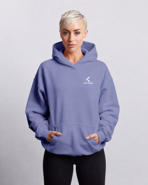 Female model wearing a violet oversized Kat Krush hoodie with hands in pockets in a clean front-facing studio shot.