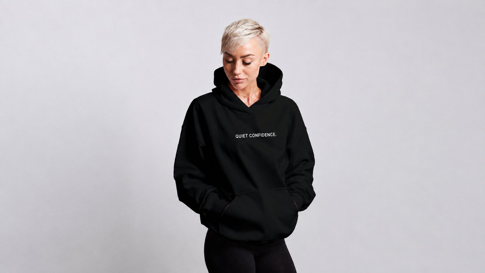 PRESS & MEDIA 2 Female model wearing a black oversized Quiet Confidence hoodie with minimalist chest branding, photographed in a clean studio setting showcasing the relaxed fit and premium streetwear design.