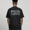 kk-tee-bristol-black-back-casual Black oversized Bristol coordinates T-shirt featuring Bristol city coordinates printed on the back, worn by a model standing with hands in pockets against a neutral studio background.