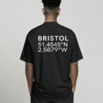 kk-tee-bristol-black-back-casual Black oversized Bristol coordinates T-shirt featuring Bristol city coordinates printed on the back, worn by a model standing with hands in pockets against a neutral studio background.
