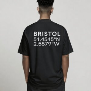 Black oversized Bristol coordinates T-shirt featuring Bristol city coordinates printed on the back, worn by a model standing with hands in pockets against a neutral studio background.