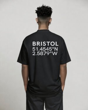 Black oversized Bristol coordinates T-shirt featuring Bristol city coordinates printed on the back, worn by a model standing with hands in pockets against a neutral studio background.