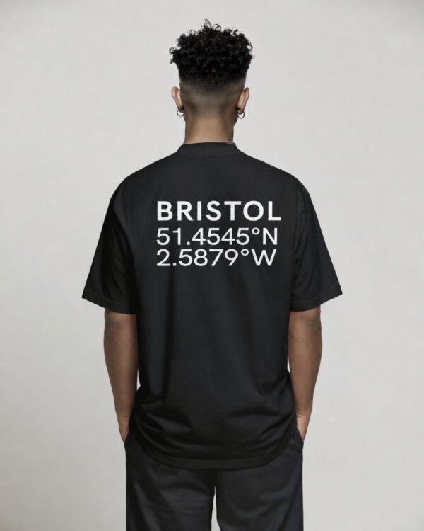 kk-tee-bristol-black-back-casual Black oversized Bristol coordinates T-shirt featuring Bristol city coordinates printed on the back, worn by a model standing with hands in pockets against a neutral studio background.