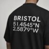 kk-tee-bristol-black-back-close-coordinates Close-up of Bristol coordinates back print on a black oversized streetwear T-shirt, showing the city name and geographic coordinates in white typography.