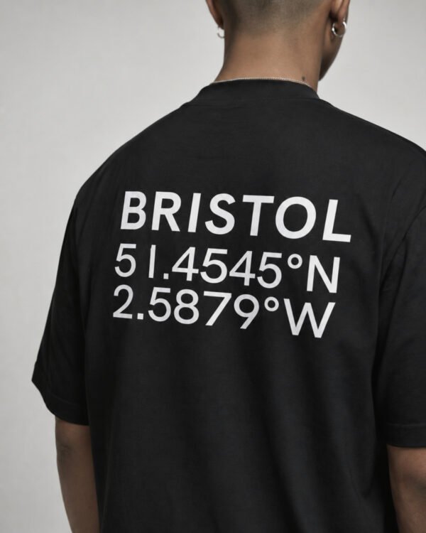 kk-tee-bristol-black-back-close-coordinates Close-up of Bristol coordinates back print on a black oversized streetwear T-shirt, showing the city name and geographic coordinates in white typography.