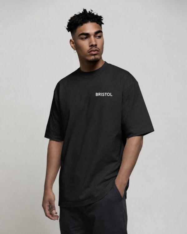 kk-tee-bristol-black-front-logo Model wearing a black oversized Bristol T-shirt featuring a minimal Bristol logo printed on the left chest in a clean streetwear style.