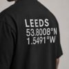 Close-up of Leeds coordinates typography printed on the back of a black oversized T-shirt, highlighting the minimalist city-inspired design.