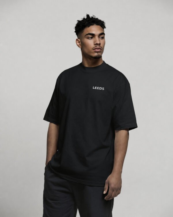 Black oversized Leeds T-shirt with small Leeds chest logo, worn by a model in a relaxed pose against a neutral studio background.