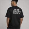 Waist-up back view of a black Leeds coordinates T-shirt displaying large white city coordinates in a clean minimalist layout.
