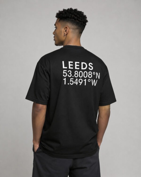 Waist-up back view of a black Leeds coordinates T-shirt displaying large white city coordinates in a clean minimalist layout.