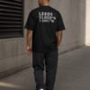 Model walking through a contemporary concrete environment wearing a black Leeds coordinates T-shirt with oversized streetwear fit and back print.