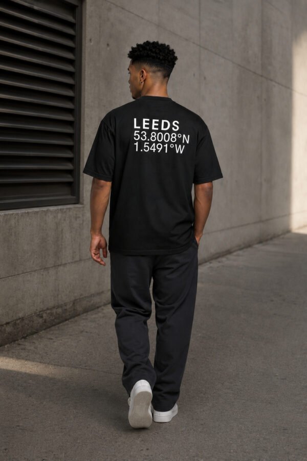 Model walking through a contemporary concrete environment wearing a black Leeds coordinates T-shirt with oversized streetwear fit and back print.