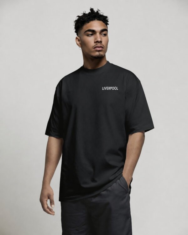 Model wearing a black oversized Liverpool T-shirt with subtle Liverpool chest logo and clean minimalist streetwear styling.