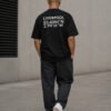 Model wearing a black Liverpool coordinates T-shirt in a minimalist concrete setting, showing the oversized fit and rear city print.