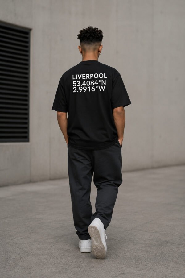 Model wearing a black Liverpool coordinates T-shirt in a minimalist concrete setting, showing the oversized fit and rear city print.