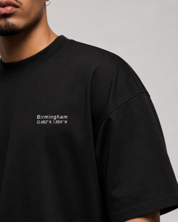 Close-up of the Birmingham Signature chest print on a black oversized heavyweight T-shirt showing premium cotton fabric and clean white coordinates design.